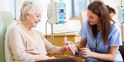 Patient sitting in a chair while a nurse sorts out a chemotherapy tube in their hand.