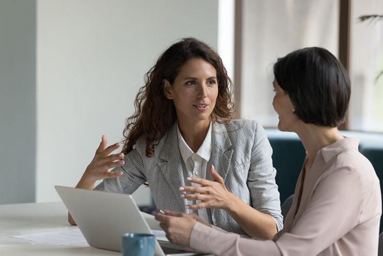 Two women talking to one another with a laptop infront of them